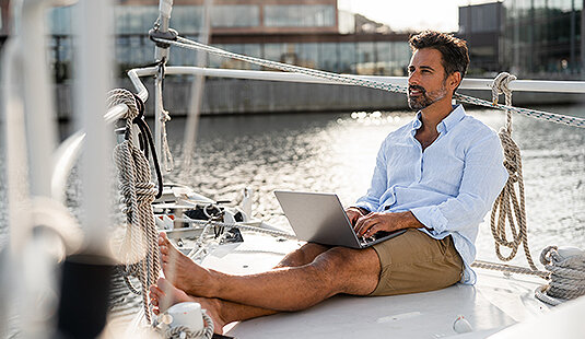 Ein freier Makler, der mit seinem Laptop entspannt an Deck eines Segelbootes sitzt