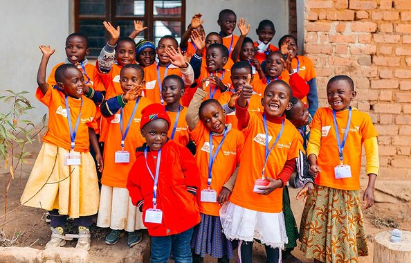 Fröhliche Kinder aus dem Wunschpatenprogramm von World Vision in Tansania winken lachend in die Kamera