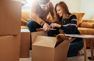 Ein junges Paar beim Auspacken von Umzugskartons in ihrer Wohnung als Mood-Foto für private und gewerbliche Sachversicherungen