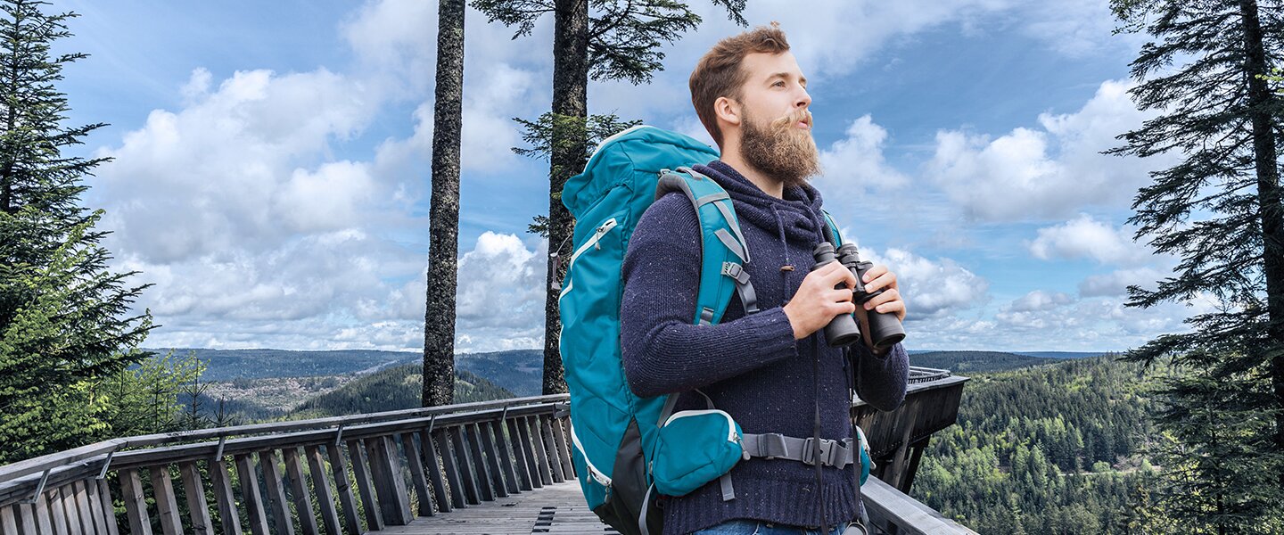 Ein Wanderer mit Rucksack auf einer Aussichtsplattform im Wald als Imagebild für News im Bereich Baufinanzierungen