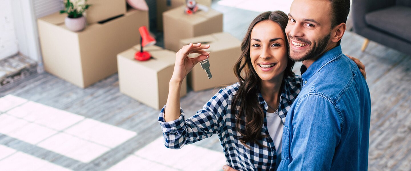 Ein gut gelauntes Pärchen, das den Schlüssel zu ihrer neuen Wohnung in den Händen hält