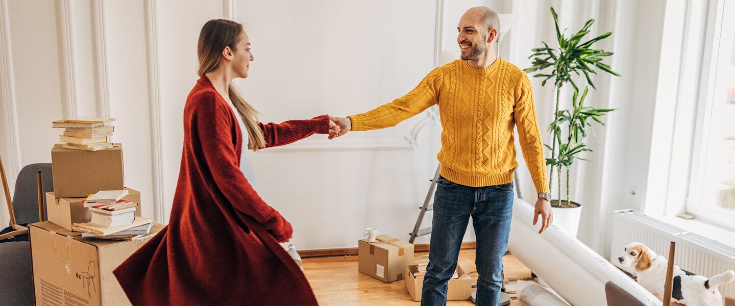 Ein Pärchen, das einer Wohnung per Baufinanzierung finanziert hat und nun dort fröhlich zwischen Umzugskartons tanzt