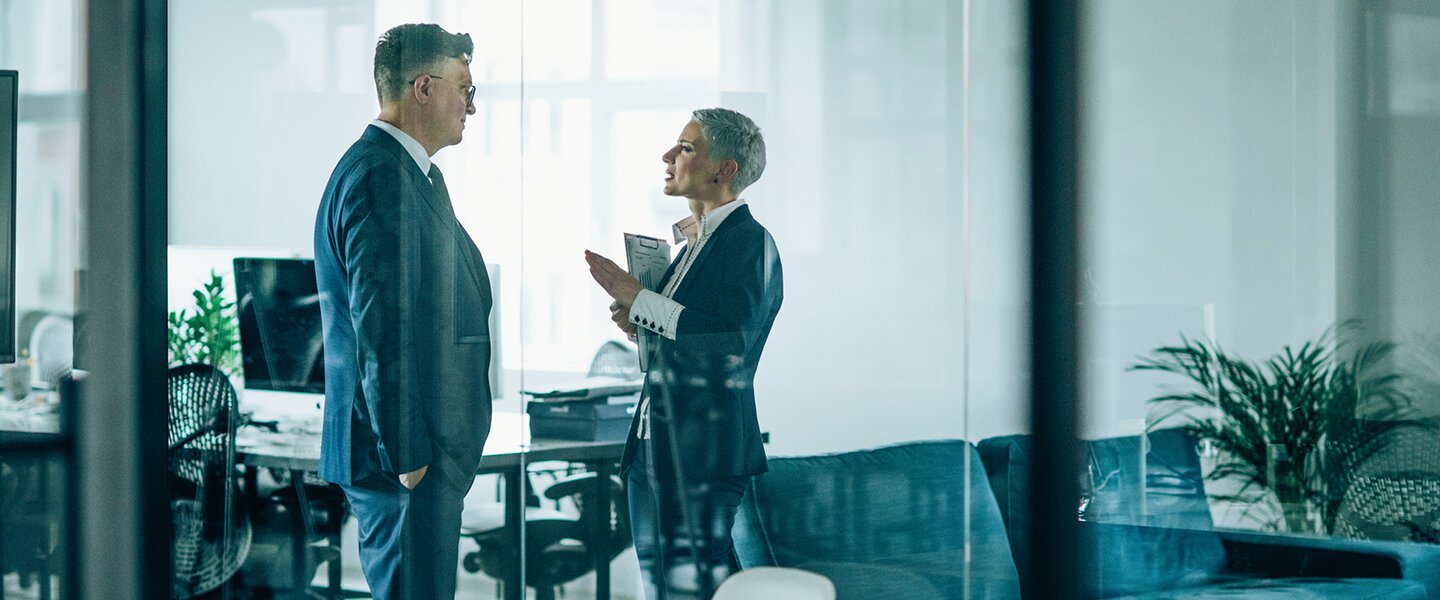 Zwei Vermittler im Büro, die sich über die Falleinreichung bei Baufinanzierungen unterhalten sowie Tipps austauschen, wie sich Kreditablehnungen für Kunden vermeiden lassen