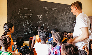 Simon aus dem CSR-Team der Fonds Finanz zusammen mit Schulkindern an der Tafel im Klassenzimmer