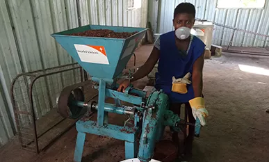 Eine Frau arbeitet für die Herstellung von Sheabutter an einer Maschine mit großem Trichter