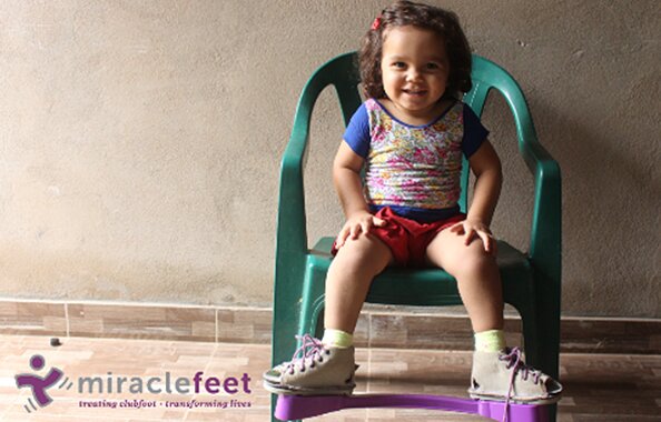 Bild von der gemeinnützigen Organisation Miracle Feet mit einem kleinen Mädchen, das lächelnd auf einem Stuhl sitzt