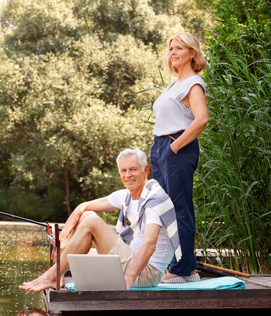 Bestager-Paar auf einem Bootssteg informiert sich am Laptop über die Absicherung ihrer Arbeitskraft